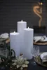 Three white LED candles are lit on a dark table, set for an outdoor evening gathering. Produktbild-Vorschau