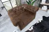 A brown Chesterfield armchair is shown in a room with a large window and a cowhide rug. Náhled obrázku produktu