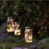 Three mason jar lanterns with fairy lights hang from tree branches. Produktbild-Vorschau