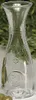 A clear glass carafe with embossed text and a circular emblem on a background of greenery and white. Produktbild-Vorschau