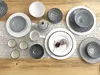A collection of ceramic tableware, including plates, bowls, cups, and a teapot, arranged on a wooden table with a lace runner. Produktbild-Vorschau