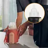 A person is placing a baby bottle into a pink and black bottle warmer, which is next to a black bag. Produktbild-Vorschau