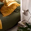 A bed with green and yellow bedding, with a lamp on a stack of magazines next to it. Podgląd zdjęcia produktu