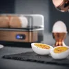 A breakfast set featuring an egg cooker and toaster, with sliced eggs in the foreground. Produktbild-Vorschau