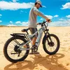 A man stands with an electric bicycle on a sandy beach under a blue sky with clouds. Produktbild-Vorschau