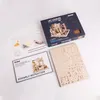 A flat lay of a model building kit, including the box, assembly instructions, and wooden pieces. Voir les images du produit