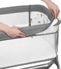 A close-up shot of a person's hands adjusting the side of a baby crib or bassinet. Produktbild-Vorschau