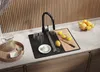 A modern kitchen sink area with a black sink, faucet, cutting board, lemons, and a pitcher of water. Produktbild-Vorschau
