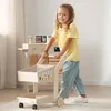A young girl is playing with a wooden toy shopping cart in a play store setting. Produktbild-Vorschau