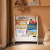 A children's bookshelf filled with books, placed in a room with a curtain and a beanbag chair. Produktbild-Vorschau