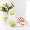 A still life arrangement featuring a bouquet of tulips, three food storage containers with green lids, a loaf of bread, two white Easter bunnies, and a small wooden spoon and scoop. Náhľad obrázku produktu