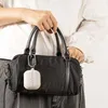 A person is holding a black handbag with a white earbud case attached to it. Produktbild-Vorschau