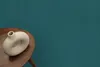 A beige donut-shaped vase sits on a round wooden table against a teal textured background. Voir les images du produit