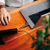 A person's hand is using a mouse next to a laptop with a USB drive plugged in. Náhľad obrázku produktu