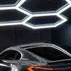 A dark, modern garage or workshop with hexagonal LED ceiling lights illuminating a sleek, dark-colored car. Náhled obrázku produktu