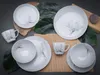 A set of white porcelain dishes with a floral pattern, arranged on a dark gray surface with green leaves and a bamboo placemat. Náhľad obrázku produktu