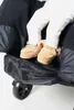 A close-up view of a baby's feet in tan moccasin-style slippers, tucked into a black stroller or carrier. Produktbild-Vorschau