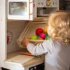 A child is playing with a wooden toy kitchen set, arranging toy fruits and vegetables in a basket. Náhľad obrázku produktu