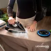 A person is ironing clothes on an ironing board, with steam coming from the iron. A charging base for the iron is also visible. Produktbild-Vorschau