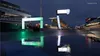 A racing circuit at night with wet asphalt reflecting the lights of the grandstands and advertising boards. Produktbild-Vorschau