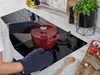 A person is using oven mitts to place a red pot on a modern induction stovetop in a kitchen. Produktbild-Vorschau