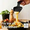 A person is using a raclette grill to melt cheese over food, with a plant and a salt/pepper grinder in the background. Produktbild-Vorschau
