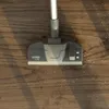 A close-up of a vacuum cleaner head on a wooden floor with some debris. Voir les images du produit