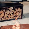 A black metal firewood rack filled with logs sits on a tiled patio next to a fire pit with flames. Podgląd zdjęcia produktu