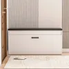 A white shoe cabinet with a black top and a single drawer, placed on a rug in a hallway. A pair of slippers is on the rug in front of the cabinet. Podgląd zdjęcia produktu