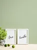 Two framed pictures with text on a wooden surface, next to a potted plant and limes. Produktbild-Vorschau