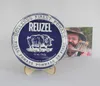 A Reuzel Fiber Pomade tin is displayed on a wooden stand, with a photograph of a man in the background. Podgląd zdjęcia produktu