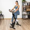A woman is exercising on a stationary bike in a room with wooden floors and shelves in the background. Náhľad obrázku produktu