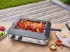 A rotisserie grill with chicken and vegetables cooking on it, placed on a wooden deck outdoors. Produktbild-Vorschau