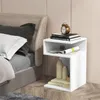 A white S-shaped nightstand next to a bed, decorated with books, vases, and an alarm clock. Podgląd zdjęcia produktu