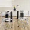 Two clear folding chairs are placed in front of a modern dining table with a vase of flowers. Produktbild-Vorschau