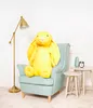 A large yellow plush bunny sits in a light blue armchair next to a floor lamp and small side tables. Podgląd zdjęcia produktu