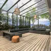 An outdoor lounge area with a large sectional sofa, coffee table, and ottoman under a glass roof. Produktbild-Vorschau