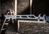 A close-up of a reciprocating saw blade resting on insulation material, with a ladder and wooden structure in the background. Voir les images du produit
