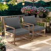 Two dark gray outdoor cushions on wooden rocking chairs on a patio, with potted flowers and hanging lanterns in the background. Náhled obrázku produktu