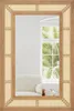 A mirror with a rattan frame reflecting a room with a sofa and a window with palm trees outside. Podgląd zdjęcia produktu