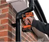 A person is using a Black & Decker cordless drill to drill a hole in a downspout attached to a brick wall. Produktbild-Vorschau