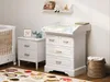 A nursery room with a changing table and a crib. Produktbild-Vorschau