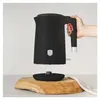 A hand holding a black electric kettle above its base, which rests on a wooden board. Náhľad obrázku produktu