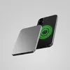 A gray power bank is shown next to a black smartphone, with a green glowing circular pattern on the back of the phone indicating wireless charging. Produktbild-Vorschau
