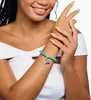 A woman's arm wearing a turquoise beaded bracelet with a peace sign and a blue camper van charm. Náhled obrázku produktu