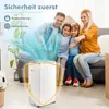 A family is sitting on a couch in a living room, with a white dehumidifier in the foreground. Blue light emanates from the dehumidifier, creating a protective shield effect. Produktbild-Vorschau