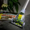 A vacuum cleaner head is shown cleaning a dark gray fabric surface, with magazines and plants blurred in the background. Voir les images du produit
