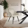 A cream-colored armchair with black legs is placed on a rug next to a black dining table in a room with a plant and a cabinet. Produktbild-Vorschau
