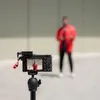 A camera is set up on a tripod, filming a person in a red jacket. Náhľad obrázku produktu