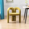 A yellow velvet chair is placed on a wooden floor next to a white table with a vase of flowers and some muffins. Voir les images du produit